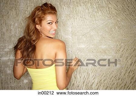 Stock Image - Young woman in tube top, looking over shoulder at camera. Fotosearch