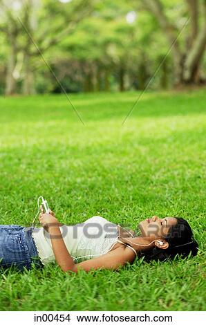 Young woman listening to music with headphones, lying on grass View Large Photo Image Picture - Young woman listening to music with headphones, lying on grass. Fotosearch