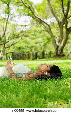 Young woman lying on grass, listening to music with headphones View Large Photo Image Stock Photography - Young woman lying on grass, listening to music with headphones. Fotosearch