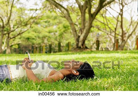 Young woman lying on grass with headphones View Large Photo Image Stock Photograph - Young woman lying on grass with headphones. Fotosearch
