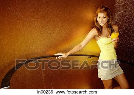 Young woman standing, holding drink, looking at camera View Large Photo Image Stock Photograph - Young woman standing, holding drink, looking at camera. Fotosearch