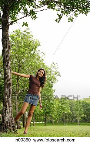 Young woman standing with hand on tree, smiling at camera View Large Photo Image Stock Image - Young woman standing with hand on tree, smiling at camera. Fotosearch