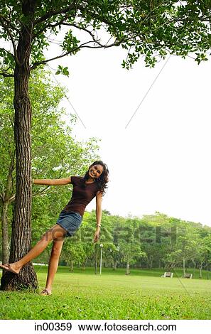 Young woman standing with hand on tree, smiling at camera View Large Photo Image Stock Photo - Young woman standing with hand on tree, smiling at camera. Fotosearch