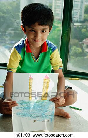 Stock Image - Boy sitting on floor, holding a drawing towards camera. Fotosearch