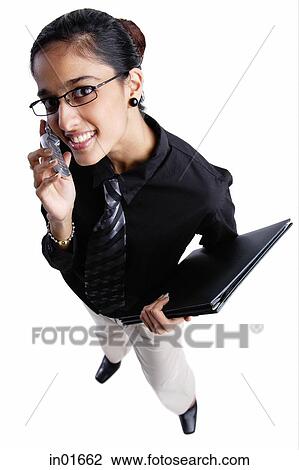 Stock Image - Business woman using mobile phone, smiling at camera, high angle view. Fotosearch