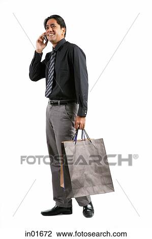 Stock Image - Businessman carrying shopping bags, talking on mobile phone. Fotosearch