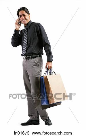 Businessman carrying shopping bags, talking on mobile phone, smiling at camera View Large Photo Image Stock Image - Businessman carrying shopping bags, talking on mobile phone, smiling at camera. Fotosearch