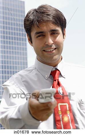 Businessman holding mobile phone towards camera, smiling View Large Photo Image Stock Photo - Businessman holding mobile phone towards camera, smiling. Fotosearch