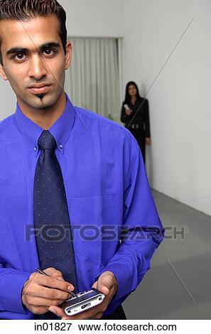Businessman holding PDA, woman in the background View Large Photo Image Stock Photo - Businessman holding PDA, woman in the background. Fotosearch