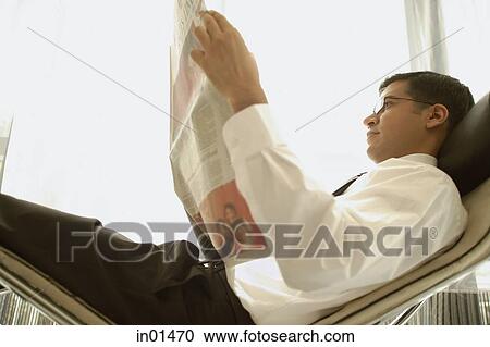 Stock Image - Businessman reclining on chair, reading newspaper. Fotosearch