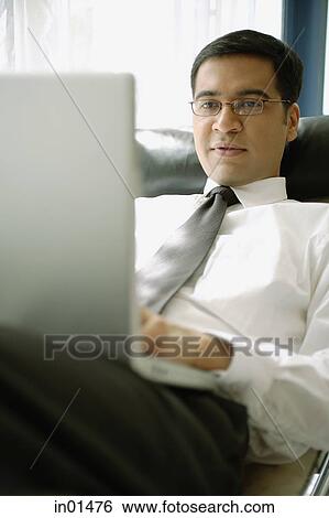 Businessman reclining on chair with laptop View Large Photo Image Stock Photograph - Businessman reclining on chair with laptop. Fotosearch
