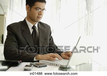 Stock Photo - Businessman sitting at desk, using laptop. Fotosearch