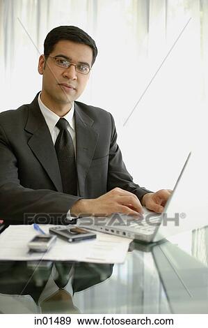 Businessman sitting at desk with laptop, PDA and mobile phone View Large Photo Image Stock Photo - Businessman sitting at desk with laptop, PDA and mobile phone. Fotosearch