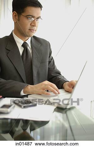 Businessman sitting at table, using laptop View Large Photo Image Stock Photo - Businessman sitting at table, using laptop. Fotosearch