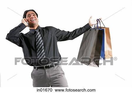 Stock Image - Businessman using mobile phone, carrying shopping bags. Fotosearch