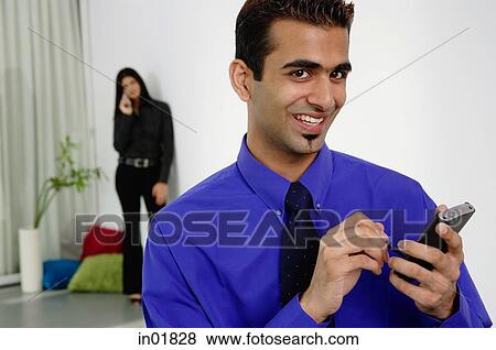 Businessman using PDA, smiling at camera, woman in the background View Large Photo Image Stock Photo - Businessman using PDA, smiling at camera, woman in the background. Fotosearch