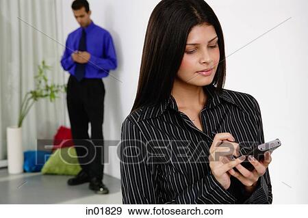 Businesswoman using PDA, man in the background View Large Photo Image Stock Photo - Businesswoman using PDA, man in the background. Fotosearch
