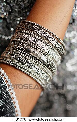 Stock Image - Close-up of woman's arm with silver bangles. Fotosearch
