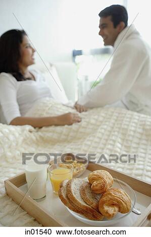 Stock Image - Couple in bedroom, breakfast tray on the bed. Fotosearch