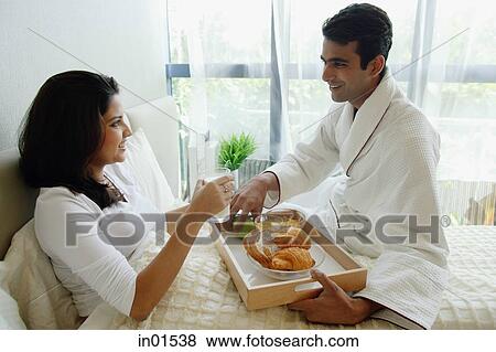 Couple in bedroom, man serving woman breakfast in bed View Large Photo Image Stock Photo - Couple in bedroom, man serving woman breakfast in bed. Fotosearch