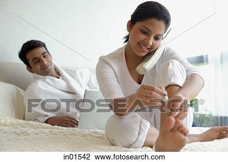 Couple in bedroom, man using laptop, woman using telephone and painting her nails View Large Photo Image Stock Image - Couple in bedroom, man using laptop, woman using telephone and painting her nails. Fotosearch