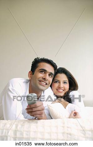 Stock Photography - Couple lying on bed, side by side, watching TV. Fotosearch