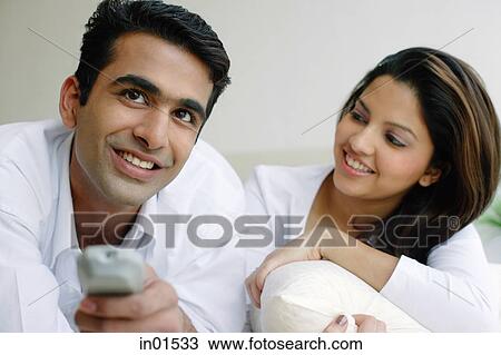 Stock Image - Couple side by side, man holding TV remote control, woman looking at him. Fotosearch
