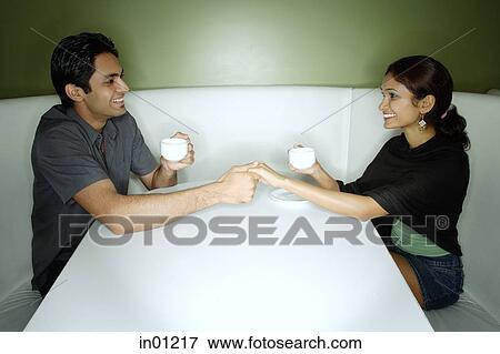 Couple sitting opposite from each other, having tea, holding hands View Large Photo Image Stock Photo - Couple sitting opposite from each other, having tea, holding hands. Fotosearch