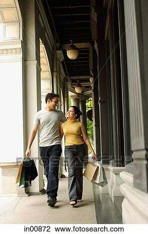 Stock Image - Couple walking, side by side, carrying shopping bags. Fotosearch