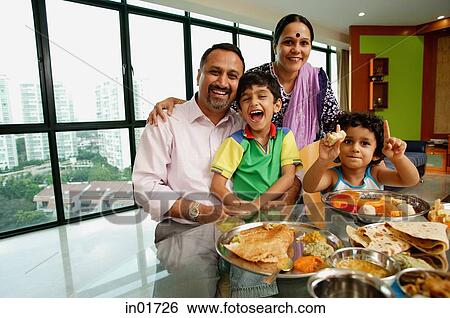 Stock Photograph - Family of four sitting around dining table, smiling at camera. Fotosearch