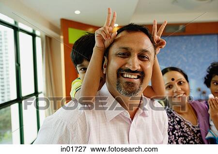 Stock Photo - Family of four smiling at camera, father carrying son on back. Fotosearch