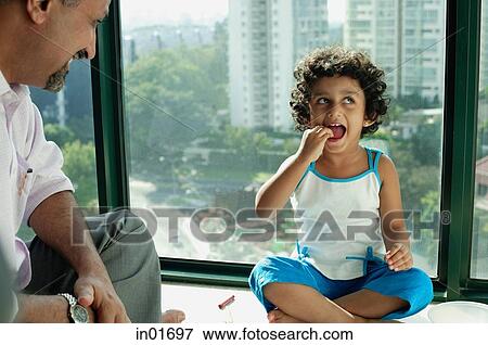 Stock Photo - Girl sitting on floor, mouth open, looking away, father sitting next to her. Fotosearch