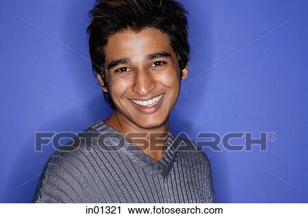 Stock Image - Man against blue background, smiling at camera. Fotosearch