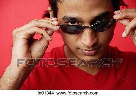 Picture - Man against red background, adjusting sunglasses, looking at camera. Fotosearch