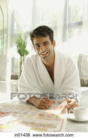 Stock Photo - Man in bathrobe, lying on floor, with newspaper, smiling at camera. Fotosearch