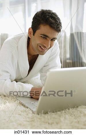 Stock Image - Man in bathrobe, using laptop, smiling. Fotosearch