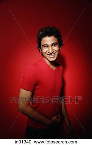 Stock Image - Man in red shirt against red background, smiling at camera. Fotosearch
