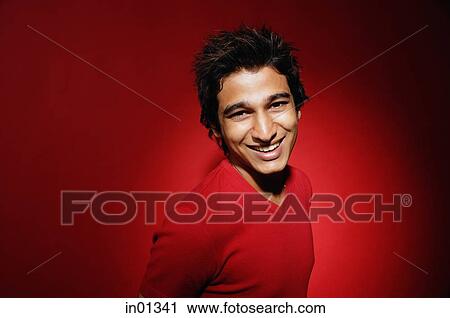 Stock Image - Man in red shirt against red background, smiling, portrait. Fotosearch