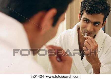 Man looking in bathroom mirror, brushing his teeth View Large Photo Image Picture - Man looking in bathroom mirror, brushing his teeth. Fotosearch