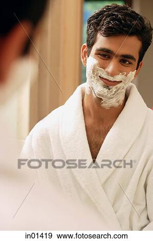 Stock Photo - Man looking in mirror having cream on face. Fotosearch