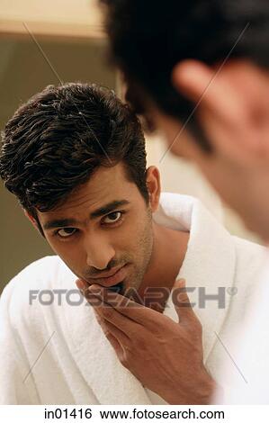 Stock Photograph - Man looking in mirror, touching his chin. Fotosearch