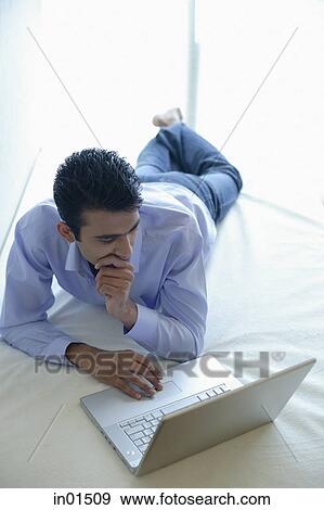 Man lying on bed using laptop, hand on chin View Large Photo Image Stock Photo - Man lying on bed using laptop, hand on chin. Fotosearch