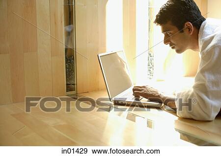 Stock Photo - Man lying on floor at home, using laptop. Fotosearch