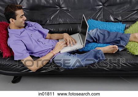 Man lying on sofa using laptop View Large Photo Image Stock Image - Man lying on sofa using laptop. Fotosearch
