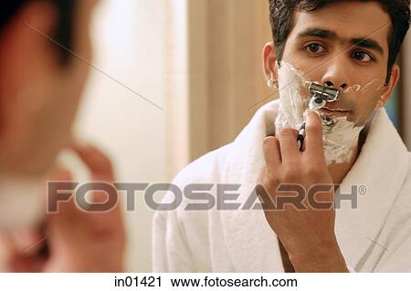 Stock Image - Man shaving his face, looking in mirror. Fotosearch