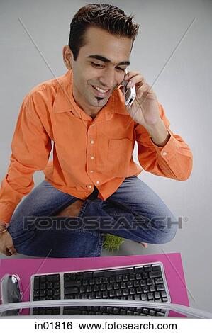 Stock Photograph - Man sitting in front of laptop, using mobile phone. Fotosearch