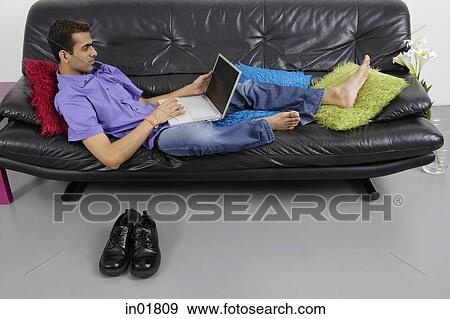 Man sitting on sofa using laptop View Large Photo Image Stock Photo - Man sitting on sofa using laptop. Fotosearch