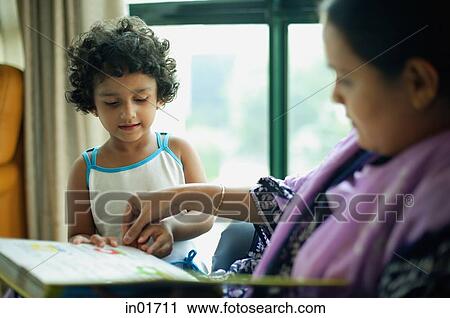 Stock Image - Mother and young daughter at home looking at photo album. Fotosearch