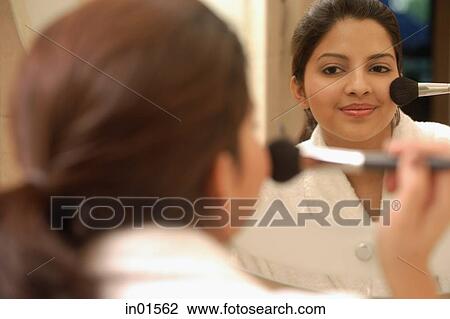 Stock Image - Woman applying blusher, looking in mirror. Fotosearch