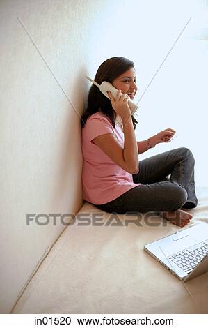 Stock Image - Woman at home, holding credit card, talking on cordless phone. Fotosearch
